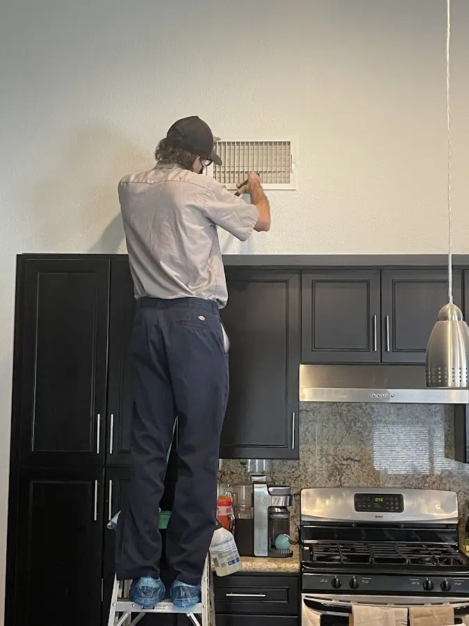 Technician inspecting an air vent during HVAC service in Henderson